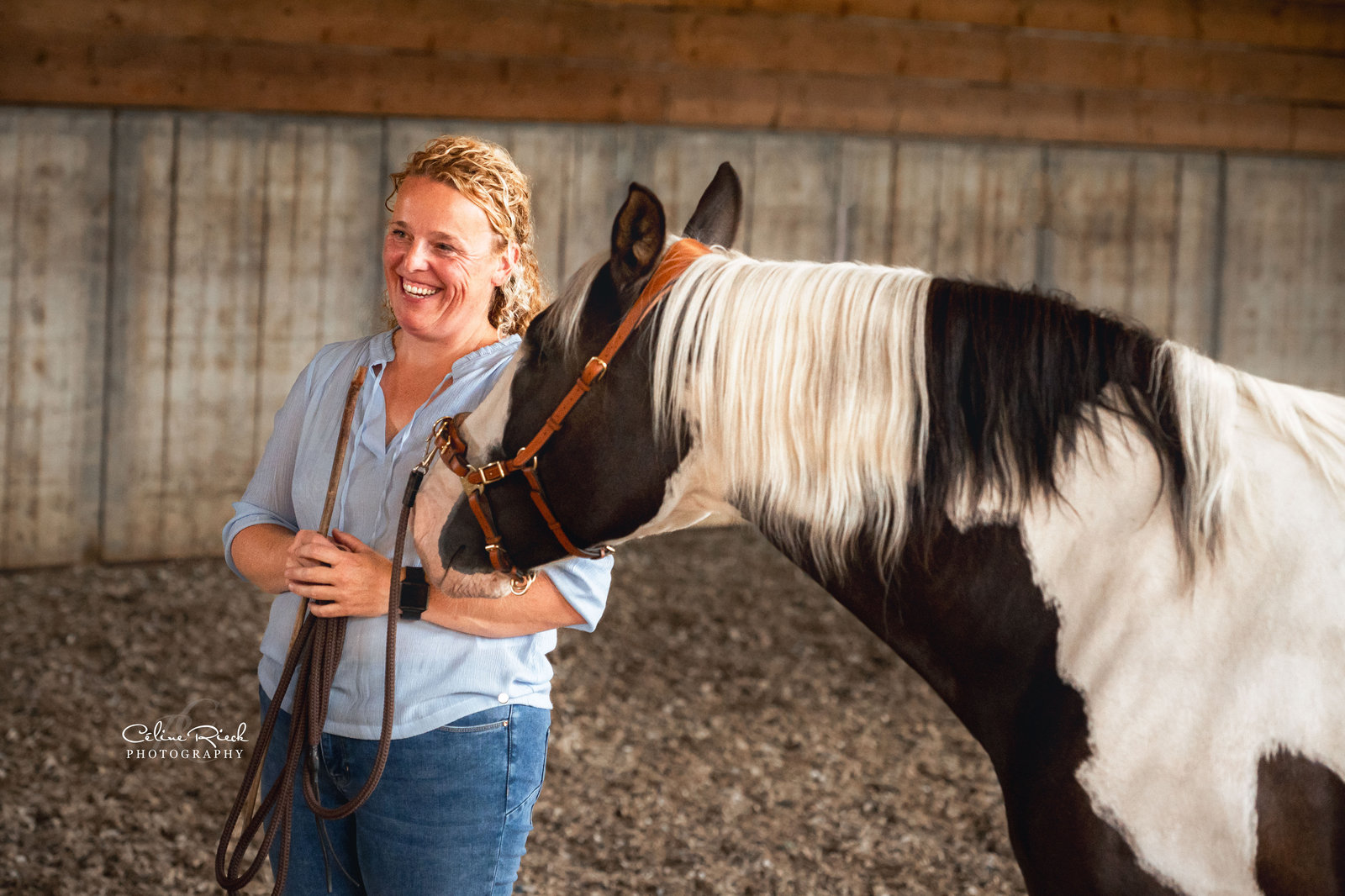 Heidi staat met longeerzweep en leadkoord naast haar bonte paard in een cavesson tijdens een training