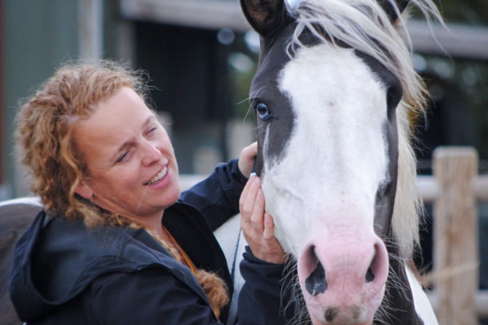 Heidi glimlacht en aait het hoofd van haar zwart-wit bonte paard langs de omheining van de weide